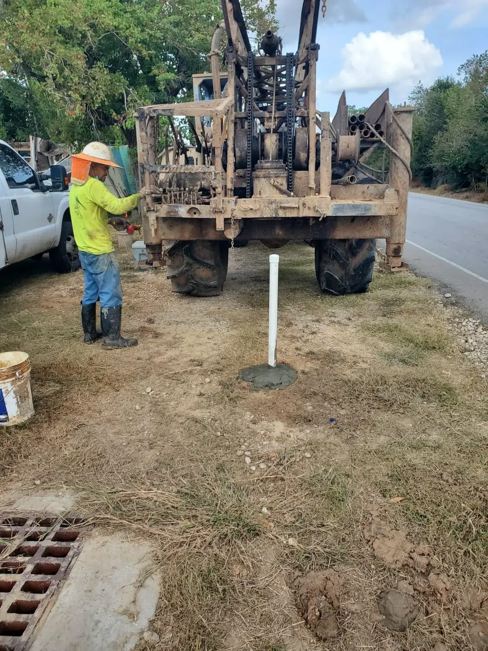 Crew operating a tall drill mast for soil borings on a grassy site