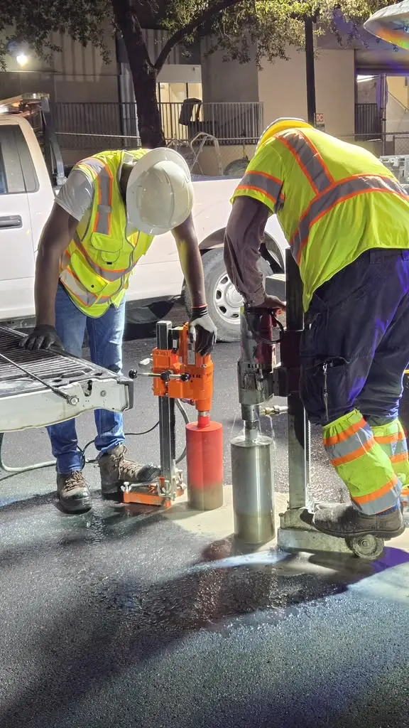 Two crew members running core drills on asphalt at night